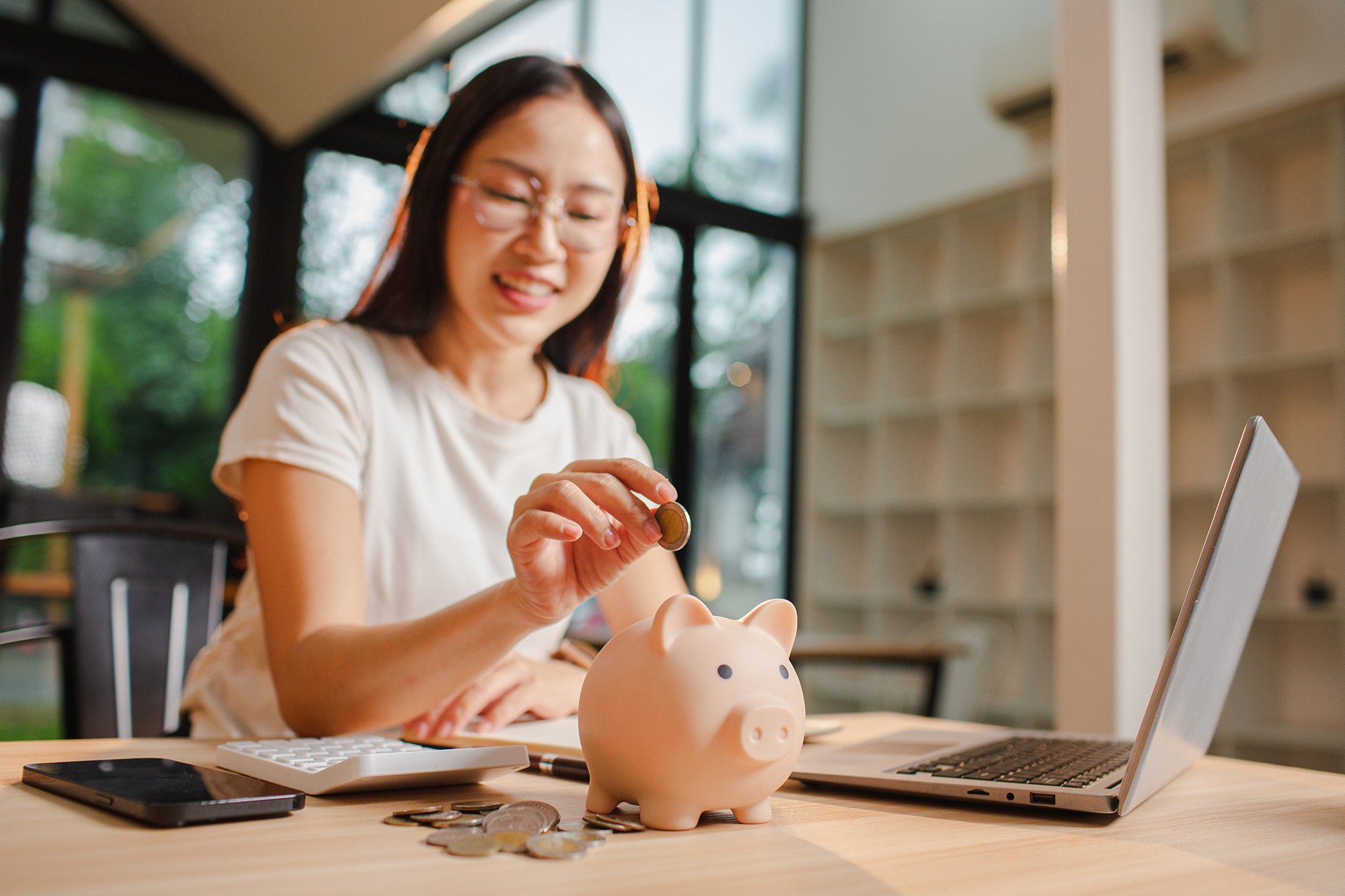 A young Asian woman saves money by putting coins in a pink piggy bank